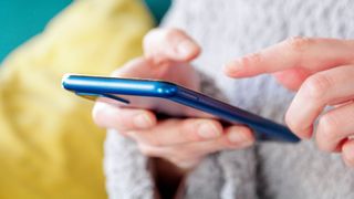 Close up of a person wearing a grey jumper using a blue iPhone