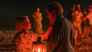 Hannah with her hand on Nathan&#039;s face as they stand by a fire on the beach at night in The Split Barcelona 