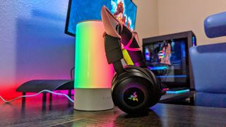 The Razer Kraken V4 Pro and Aether Lamp Pro leaning against each other on a desk with rainbow lights.