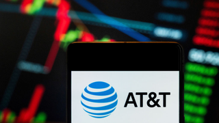 A mobile phone displays the AT&amp;T logo in front of a blurred economic stock exchange index graph in the background