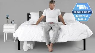 BedJet 3 Climate Comfort Sleep System on bed with white bedding and a man in white top and grey trousers sitting on it in grey room 