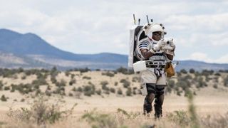 An astronaut in the desert wearing a space suit and using the Nikon Handheld Universal Lunar Camera (HULC)