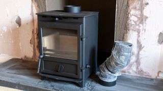 A log burner being installed with a flue beside it and a newly plastered hole in the wall behind it