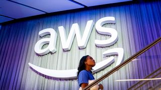 AWS logo and branding pictured at the AWS re:Invent conference at the Venetian Hotel and Casino in Las Vegas, US, with a woman walking up stairs in foreground.