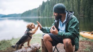 Man high fiving terrier outside on camping trip