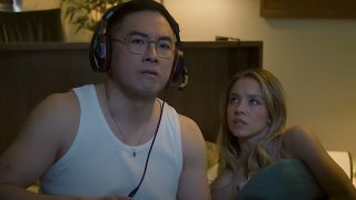 Sydney Sweeney in bed with Bowen Yang, who is wearing a headset during an SNL sketch