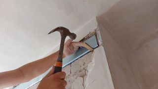 close up of hand holding hammer putting metal lintel into chimney breast