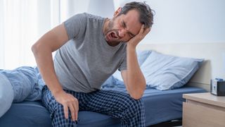 A man sits up in bed at night because restless leg syndrome is keeping him awake and is affecting his sleep