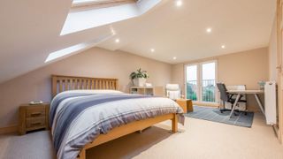 A newly converted loft room with a desk by a Juliet balcony, and a double bed under a sloping ceiling with rooflights