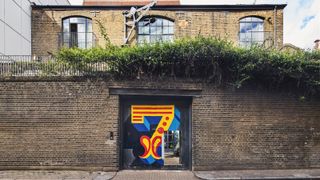 A tall brick wall in front of a house with a large metal door in the middle with the number 7 written onto it