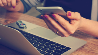 Woman on Macbook checking iPhone