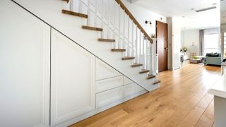 Under stairs storage with white fitted doors in a large hallway with a wooden floor