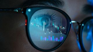 A close-up image of a woman wearing glasses, in which a banking graph is reflected, to represent open banking.