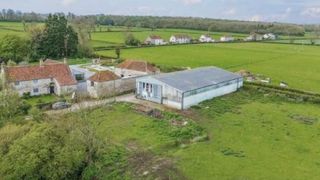 A large green building plot with an agricultural building in the middle