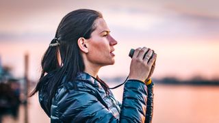 Woman holding one of the best compact binoculars against a watery sunset