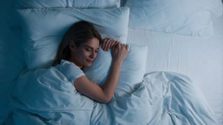 A woman with long dark hair falls asleep in bed