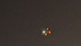 a blurry image of four lights — one white, two yellow and one orange — in the night sky