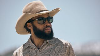 Denim Richards as Colby in Yellowston wearing his cowboy hat and sunglasses and looking to his right. 