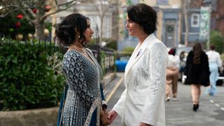 Suki and Eve standing in the Square wearing their wedding outfits - Eve has a beautiful navy dress with sequins and Eve is wearing a white sparkly suit 