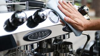 Person&#039;s hand wiping front of coffee maker with cloth