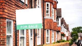 View down street of terraced houses with for sale sign on first house