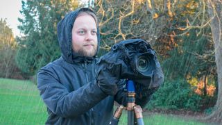 Man photographing in the rain using a tripod and camera with a rain cover