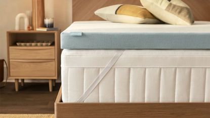 Corner of the Tempur-Adapt Tempur-Topper on a mattress atop a wooden bed frame beside a wooden nightstand. 