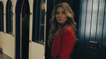 linda cardellini wears a red jacket and looks behind her while walking down a hall in no good deed