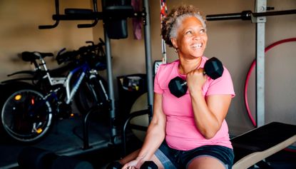 Woman sits on edge of weights bench curling one dumbbell