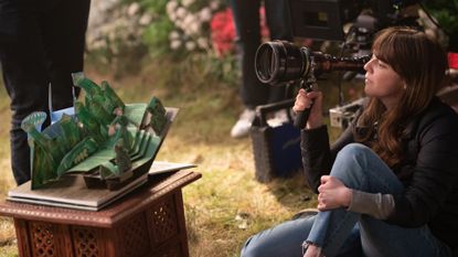 Cinematographer Alice Brooks (right) holds up a lens while filming a green miniature of a set from &#039;Wicked&#039; Part One.