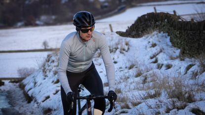 Male cyclist riding up a snowy lane wearing a pale blue long sleeved jersey