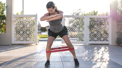 Woman in sportswear steps sideways with a resistance around her legs, just below the knees