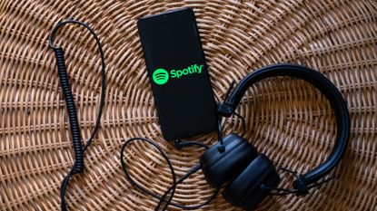 Spotify logo seen on a phone connected to a pair of headphones.