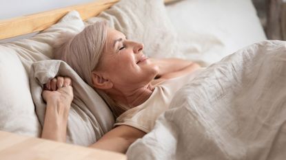 Woman lying on her back, smiling, waking up in the morning, representing can you wear a bra to bed