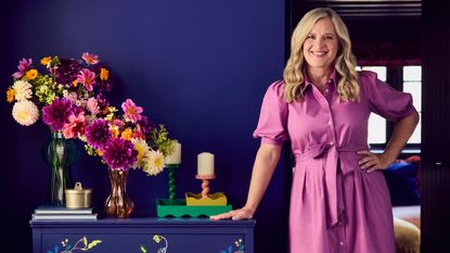 Sophie Robinson leaning against a chest of drawers from her collection for Dunelm decorated with candle holders and wavy trays from the range