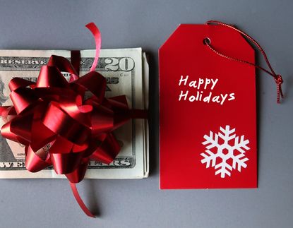 Stack of $20 bills with a red gift bow on top and a red gift tag that says &quot;Happy Holidays.&quot;