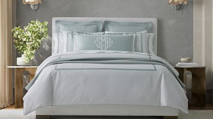 Louise Bed Sheets by Matouk on a bed against a gray wall. 