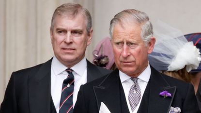 Prince Andrew wears a suit with a navy and red striped tie as he stands behind his brother King Charles, who is also wearing a suit