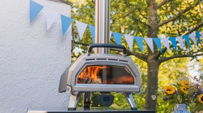 One of the best pizza ovens, an Ooni Karu 16 in a garden next to a vase with sunflowers