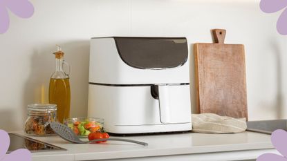 A white air fryer next to a wall and a chopping board