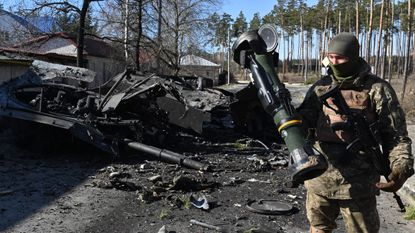 A Ukrainian soldier poses with an NLAW next to a destroyed Russian tank