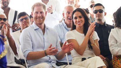 Prince Harry and Meghan Markle sitting in chairs smiling and clapping 