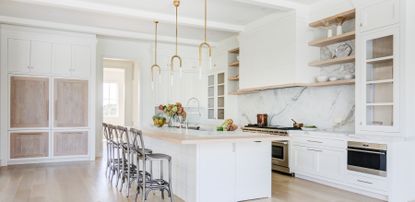 A luxury spacious white kitchen with an island, a marble splashback and light wooden finishes 