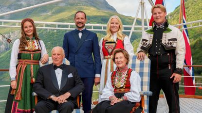 ing Harald, Queen Sonja, Crown Prince Haakon, Crown Princess Mette-Marit, Princess Ingrid Alexandra, Prince Sverre Magnus pose for a group photo aboard the kingship Norway with mountains in the background