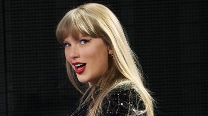 Taylor Swift poses onstage at the eras tour wearing her signature pat mcgrath red lipstick