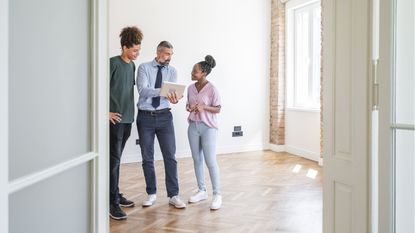 A couple of home buyers talk with a real estate agent in the front room of a vacant house.