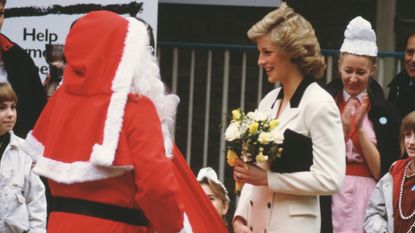 Princess Diana wearing a pale pink suit and holding flowers while talking to Santa Claus