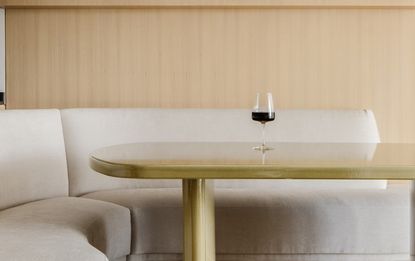 A dining table with curving sofa and a single wine glass kept atop