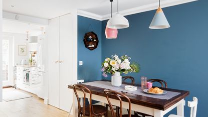 Open plan kitchen dining space with blue paint in dining area and three pastel coloured pendant lights