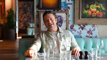 jamie oliver on banquette seat in restaurant in front of paintings and patterned wall paper